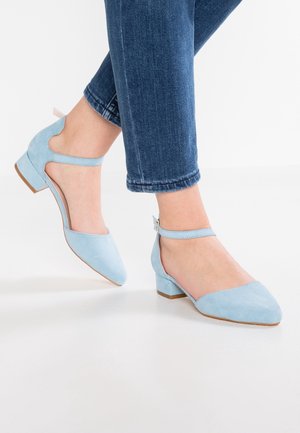 Lyseblå ruskind lavhælede sko med åbent bagdesign, ankelrem og spids tå. Flad blokhæl og kontrasterende sålefarge.
