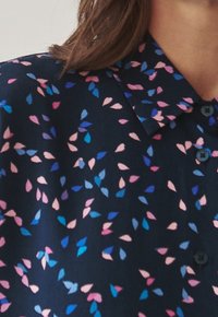 Marineblouse met een delicate bladerenpatroon in roze en blauw. Klassieke kraag, knoopsluiting aan de voorkant en lichtgewicht stof met een gladde textuur.