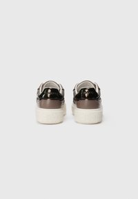 Un paio di sneaker in pelle marrone con tacco sul tallone nero lucido e suole spesse bianche a motivo, viste da dietro.