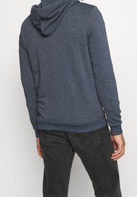 Blue heathered hoodie with a drawstring hood, ribbed cuffs, and waistband. Material is soft with a smooth texture, designed for comfort.