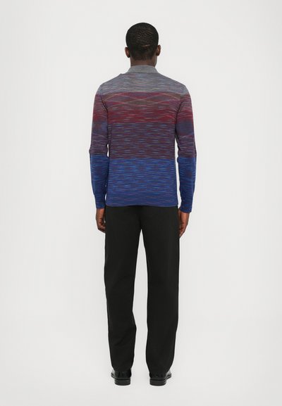 Camisa de manga longa com um design em degradê em tons de vermelho, azul e cinza, apresentando um padrão de ondas subtil; combinada com calças pretas.