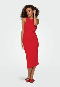 Vestito rosso a costine senza maniche con una silhouette aderente. Design a lunghezza ginocchio abbinato a scarpe rosse con fiocchi e pois.