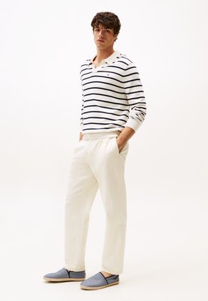 Suéter a rayas en crema y azul marino, pantalones blancos y zapatos azul claro sin cordones. Presenta un cuello con collar y puños acanalados. Diseño simple.