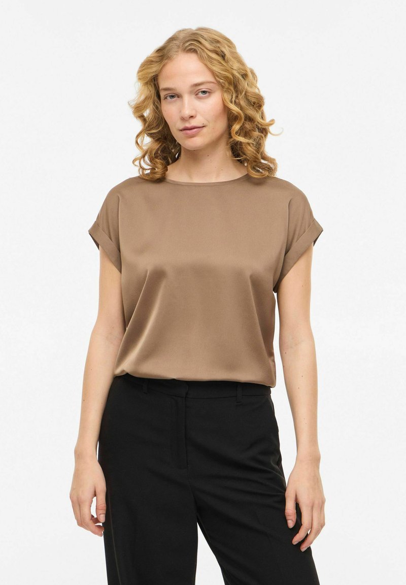 Haut en satin marron avec manches courtes retroussées, encolure ronde et coupe décontractée, associé à un pantalon noir sur mesure. Texture lisse et design minimaliste.