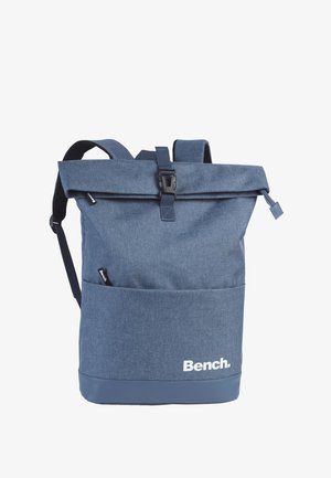 Blue fabric backpack with a roll-top closure, adjustable straps, front pocket, and a rubberized base. Features a white logo on the front.