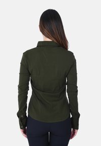 Camicia a maniche lunghe di colore verde scuro, con colletto e polsini con bottone, dal taglio sartoriale e tessuto liscio.