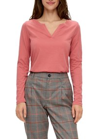 Långärmad tröja med v-ringning i mjuk korallfärgad tyg, kombinerad med grå rutiga byxor med orange detaljer och knäppning.