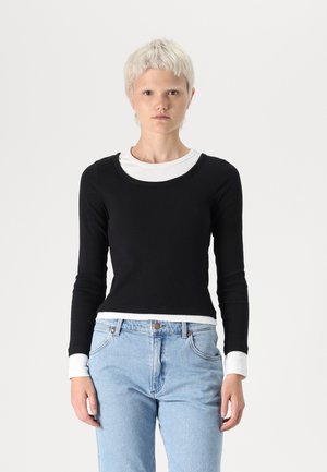 Long-sleeve black top with a scoop neck, layered over a white shirt at the collar. Made of smooth fabric, fitted design, minimalistic style.