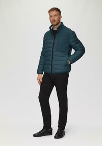 Teal pufferjack met een gewatteerd ontwerp en een hoge kraag, gecombineerd met zwarte slim-fit broek en zwarte sneakers. Heeft zijzakken en een ritssluiting.