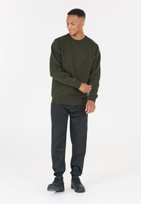 Sweatshirt vert olive avec un col rond, des poignets et un ourlet côtelés ; associé à un pantalon de survêtement noir fuselé et des baskets noires.