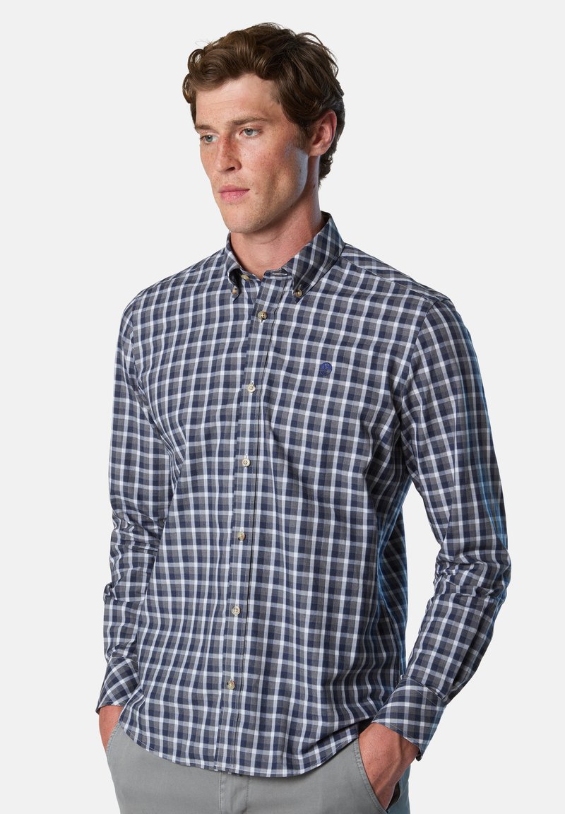 Camisa de cuadros en azul marino y azul claro, con cuello estándar y mangas largas. Presenta un bolsillo en el pecho izquierdo y botones.