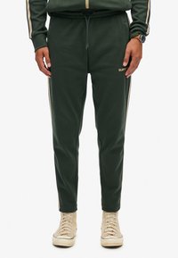 Grønne sweatpants med slim fit, der har en snøre i taljen, sidestriber i creme og et lille guld logo på venstre lår.