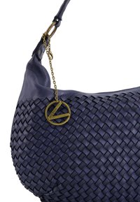 Námořnicky modrá kožená kabelka s tkanou texturou, zakřiveným tvarem a kovovými akcenty z mosazi, na které je připevněna značková visačka řetízkem.