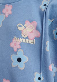 Ljusblå sweatshirt med pastellfärgade blommönster i rosa och blått. Har en vit präglad logotyp "hummel" längst ner. Mjuk textur.