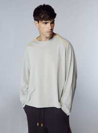 Camicia a maniche lunghe grigio chiaro con cuciture gialle lungo le spalle, realizzata in tessuto morbido. Abbinata a pantaloni neri con coulisse gialle.