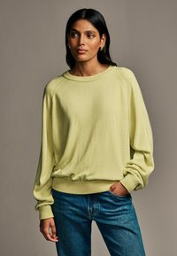 Jasnożółty, oversize sweter z prążkowanymi mankietami i dołem, w zestawie z niebieskimi dżinsami. Miękka tekstura, luźny krój i opadające ramiona.