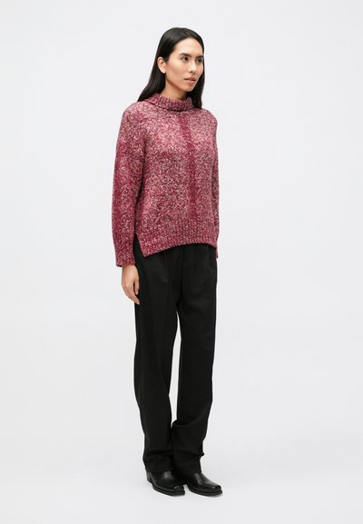 Dzianinowy pulower w odcieniach czerwieni i różu, z wysokim kołnierzem, ściągaczem w pasie i opuszczonymi ramionami, w połączeniu z czarnymi spodniami o szerokich nogawkach.