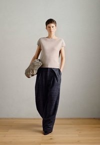 Jasnoszara bluzka z krótkim rękawem połączona z oversize'owymi spodniami w ciemną kratę. Materiał wydaje się miękki, o teksturowanym wyglądzie i luźnym, zwisającym kroju.