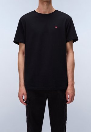 Czarna bawełniana koszulka z okrągłym dekoltem, krótkimi rękawami i małym czerwono-białym logo na piersi. Stylizowana z czarnymi spodniami.