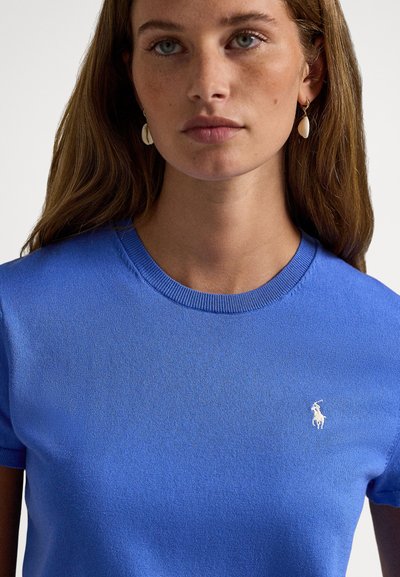 Μπλε πουλόβερ με κοντά μανίκια από υφασμένο ύφασμα, διαθέτει ριμπ λαιμόκοψη και μικρό λευκό κεντημένο λογότυπο στο στήθος.