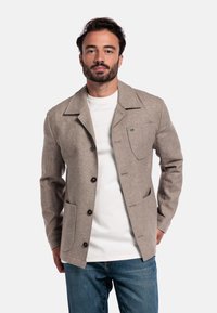 Beige wollen blazer met een reverskraag, voorzakken en donkere knopen, gecombineerd met een wit T-shirt en blauwe spijkerbroek.