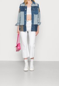Chaqueta de mezclilla con diseño de patchwork, tonos de azul claro a oscuro, top corto blanco, jeans blancos de campana, bolso rosa de imitación de cocodrilo y botas blancas.