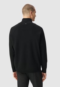 Maglione nero in maglia con colletto alto e polsini a costine, caratterizzato da un design senza cuciture e un branding minimale sul retro.
