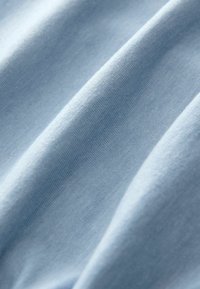 Vaaleansininen puuvillakangas, jossa on näkyvä pehmeä rakenne ja hieno ribbettimalli, esittäen lempeitä poimuja ja sileää pintaa.