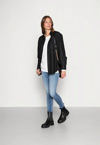 Mustast kangast nööbitav särk kahe rinnataskuga, kantud valge kampsuni peal. Kombineeritud helesiniste kitsaste teksade ja mustade massiivsete pahkluu-saabastega.