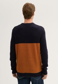 Gebreide trui met een donkerblauwe bovenhelft en een oranje onderhelft, met ribbelboorden en gestructureerde patronen over de hele trui.