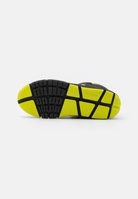 Semelle de chaussure de sport noire avec une semelle extérieure jaune vibrant. Motif texturé et rainures pour une meilleure adhérence. Marque Geox visible sur le côté.