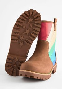 Las botas de tobillo marrones presentan un empeine de cuero suave con secciones multicolores (rojo, crema, verde, azul) y una suela de goma texturizada con patrones de estrellas.