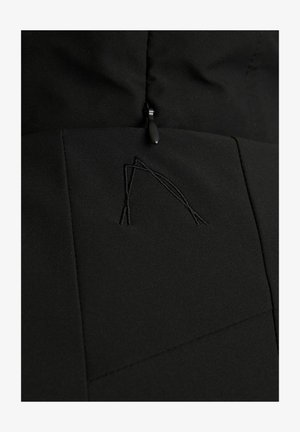 Tejido de chaqueta negra con una textura suave, con un sutil detalle bordado geométrico y un cierre con cremallera en la parte superior.