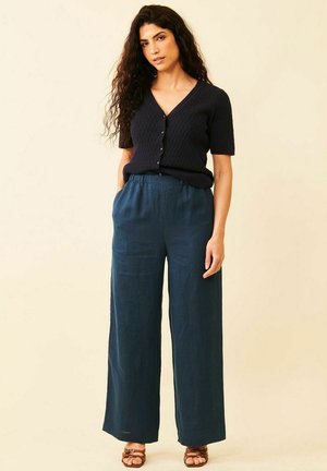 Mørkeblå ribbet cardigan med korte ærmer og knaplukning, parret med vidde ben bukser i teal, der fremhæver en afslappet pasform. Sandaler i tan med remme er inkluderet.