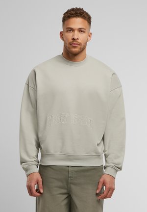 Lys grå oversized sweatshirt lavet af blødt stof, med teksten "Trust Issues" broderet i en bølget skrifttype nær bunden.