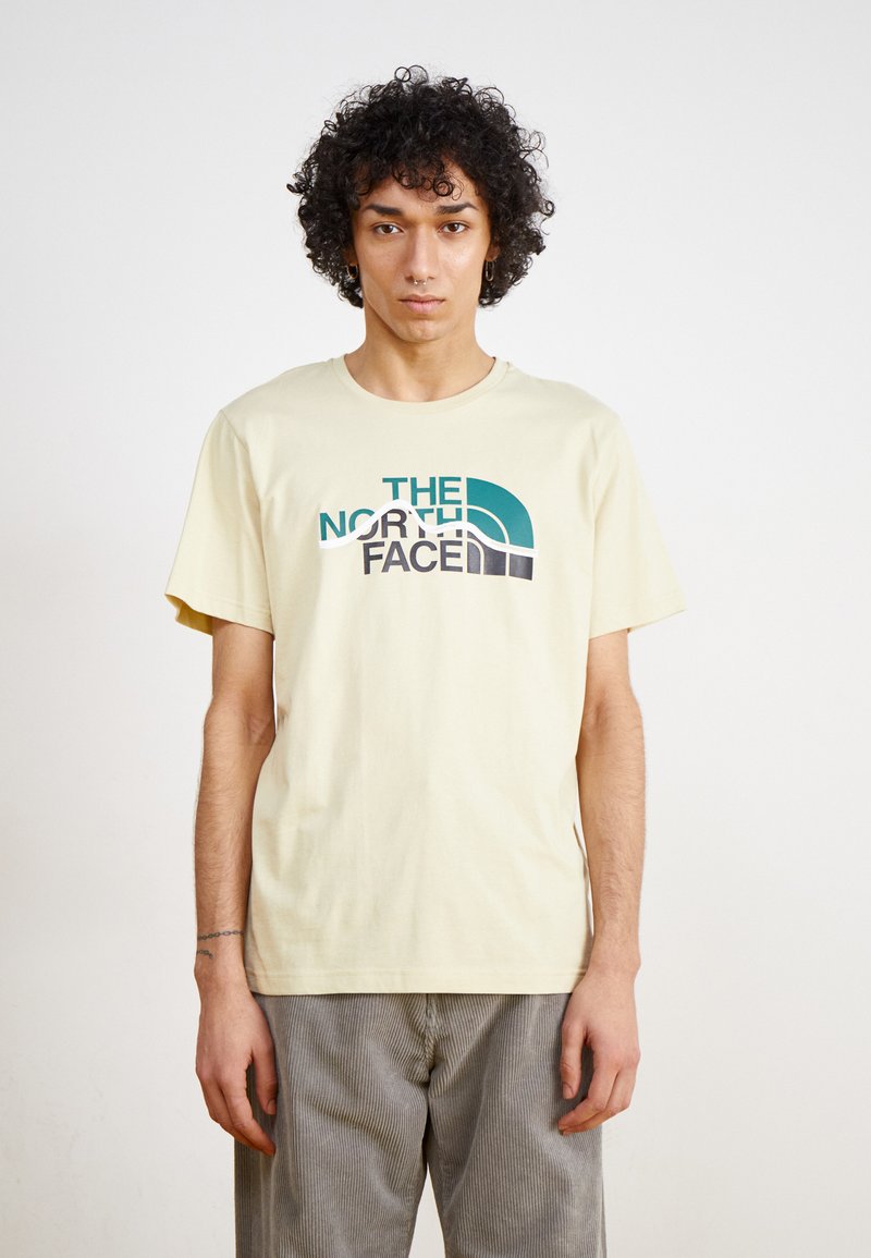 Lysegul bomulds t-shirt med et stort grafisk design i teal, grå og sort med teksten "THE NORTH FACE". Kortærmet og rund halsudskæring.