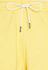 Ceinture de survêtement jaune avec cordon blanc noué en un nœud et embouts en métal aux extrémités.