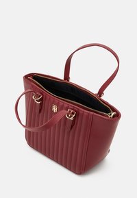 Rote synthetische Lederhandtasche mit gestepptem Muster, goldenen Hardware-Akzenten, doppelten Trägern und Reißverschlüssen, die in ein dunkles Innenfach öffnen.