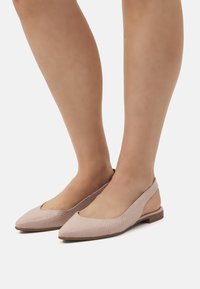 MOCASSINI BEIGE con una finitura testurizzata, punta appuntita e design con tallone aperto. Suola leggera e cinturino alla caviglia per una vestibilità sicura.