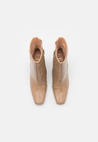 Bottes de cheville en simili cuir beige avec une texture crocodile, bout pointu et fermeture éclair sur le côté. Doublure intérieure lisse et semelle durable.