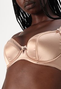 Σατιν μέσης μπεζ σουτιέν με δομημένα cups, κεντρική ανά�γλυφη κόμπο και λεπτή διακόσμηση. Διαθέτει λεία υφή και υποστηρικτικό σχέδιο.
