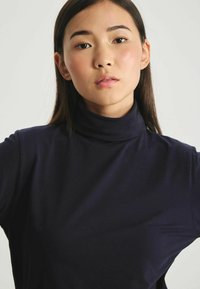 Haut col roulé marine en tissu doux et extensible. Doté d'un col haut et d'une silhouette ajustée, avec une texture lisse et un minimum de détails.