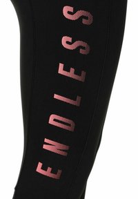 Tessuto nero con testo a pois rosa verticale che scrive "ENDLESS" lungo la manica o la gamba dei pantaloni.