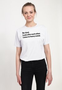 Camiseta blanca de algodón con texto negro en negrita: "Sé amable. Cuida de los demás. Escucha heavy metal." Mangas cortas, ajuste relajado.