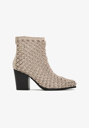 Beżowy botek za kostkę z masywnym czarnym obcasem i tkanym, teksturowanym wierzchem z plecionym wzorem, spiczastym noskiem i zamkiem błyskawicznym z tyłu.
