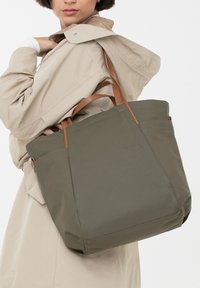 Grote olijfkleurige tote bag gemaakt van duurzaam materiaal, met bruine leren handvatten, een gestructureerd ontwerp en subtiele branding aan de voorkant.