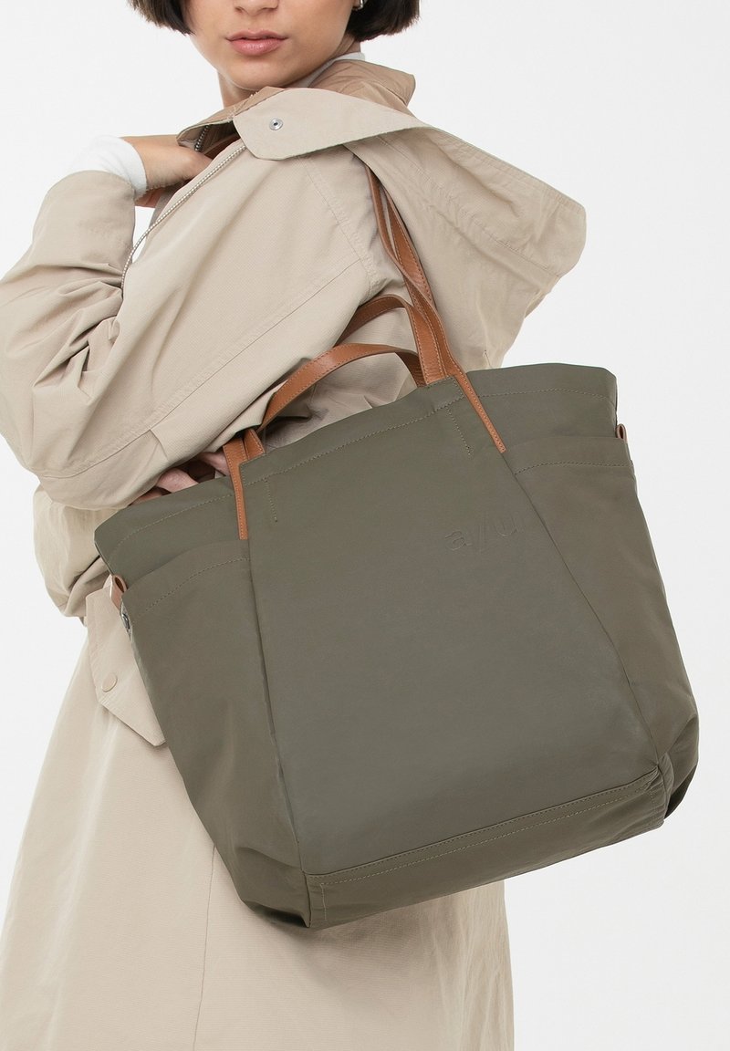 Grote olijfkleurige tote bag gemaakt van duurzaam materiaal, met bruine leren handvatten, een gestructureerd ontwerp en subtiele branding aan de voorkant.