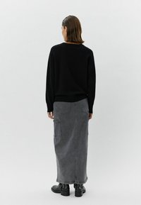 Pulover negru cu mâneci lungi, asociat cu o fustă maxi din denim gri, cu buzunare laterale și croială dreaptă, purtată cu cizme negre până la gleznă.