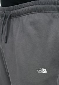 Γκρι φόρμα με ελαστική μέση και κορδόνια, με λευκό κεντημένο λογότυπο The North Face στον άνω μηρό.