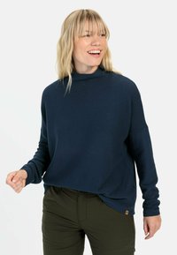 Marineblauwe, geribbelde pullover trui met een hoge hals, lange mouwen en een loose fit. Heeft een klein merklabel op de zoom.